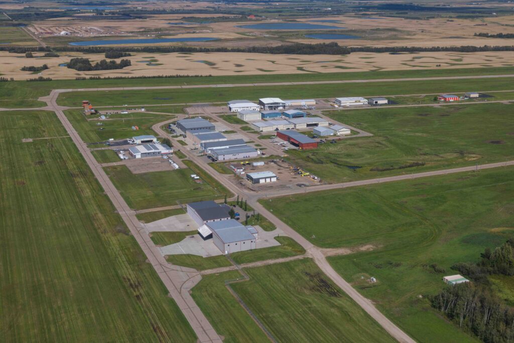Aerial view of a cluster of hangar buildings and access roads at Villeneuve Airport, with the runway and farmland beyond