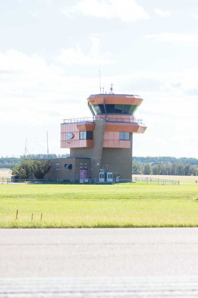 Vue d’ensemble de la tour de contrôle de l’aéroport de Villeneuve s’élevant au-dessus de la piste et de la lisière d’arbres