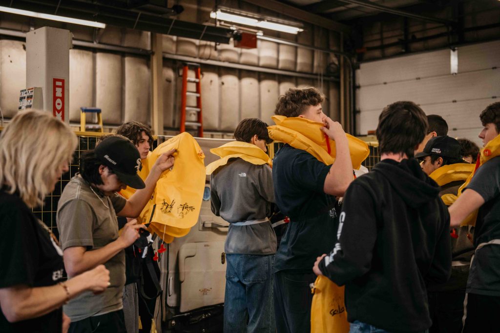 Students putting on yellow survival life vests during a training exercise in a hangar as part of the ZVL Aviation Pathway Program