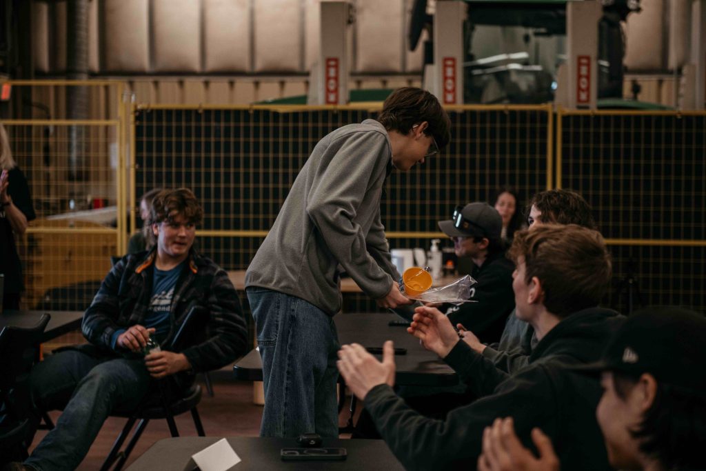 Instructor demonstrating a folded orange survival kit to seated students in a hangar during the ZVL Aviation Pathway Program